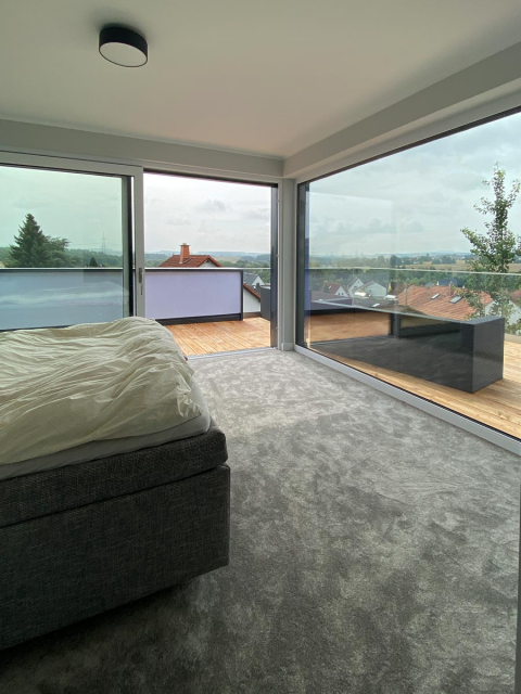 Das geräumige Schlafzimmer bietet durch die großzügigen Fenster eine beeindruckende Aussicht auf die Dachterrasse. 