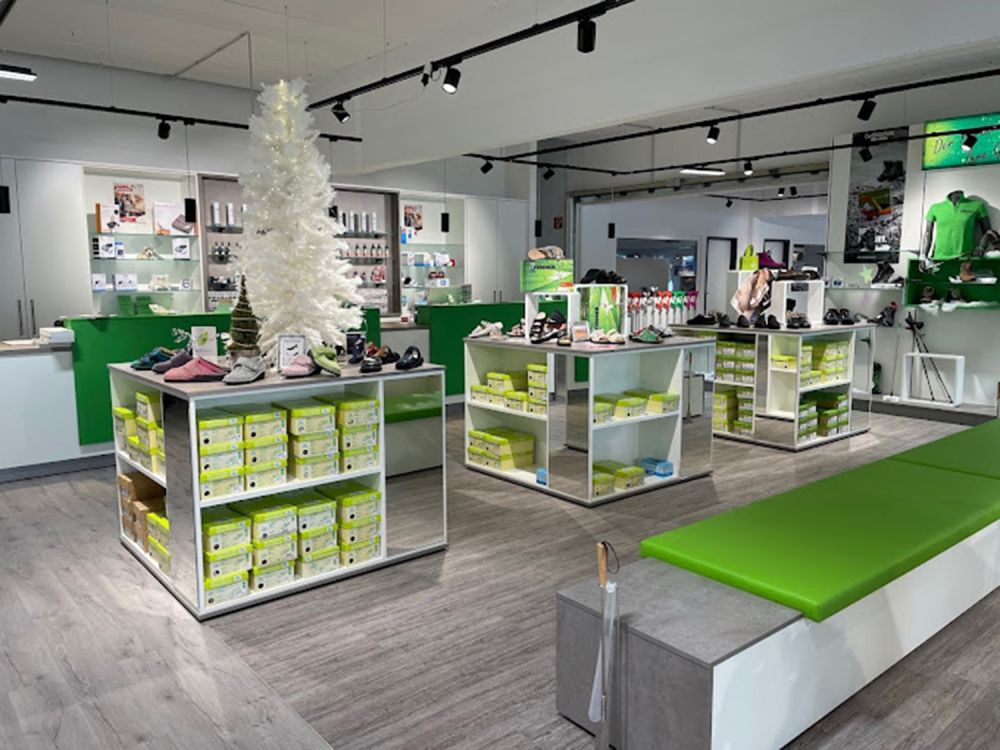 Innenansicht eines modern gestalteten Sanitätshauses in Grüntönen. Die Einrichtung ist großzügig und übersichtlich angeordnet. Im Vordergrund befindet sich ein einladender Sitzbereich mit bequemen Sesseln. Regale und Präsentationsflächen sind klar strukturiert und gut zugänglich. Die harmonische Farbgestaltung in verschiedenen Grüntönen vermittelt eine ruhige, freundliche Atmosphäre.